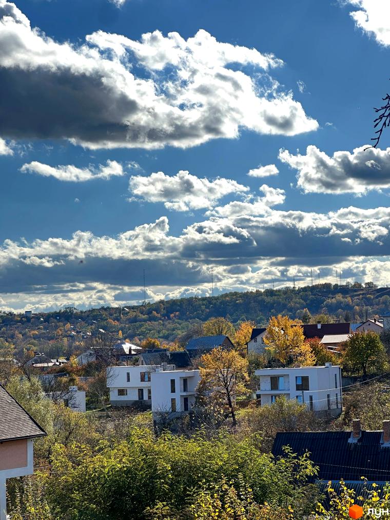 Білі будинки з великими вікнами на тлі осіннього пейзажу. Містечко котеджів Hillside розташоване серед зелені дерев та кущів.