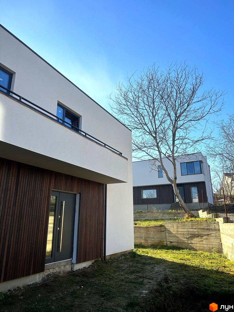 Фасад будинку в Котеджному містечку Hillside з панорамними вікнами та дерев'яним оздобленням. На території є зелена зона та дерева.