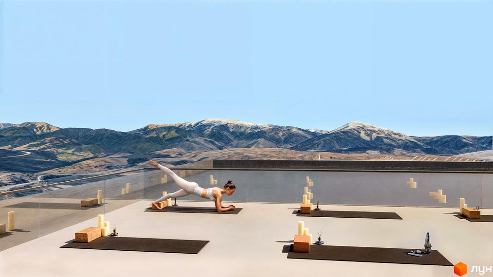 Жінка займається йогою на терасі апарт-готелю з панорамним видом на гори. На терасі розташовані килимки для йоги та свічки.