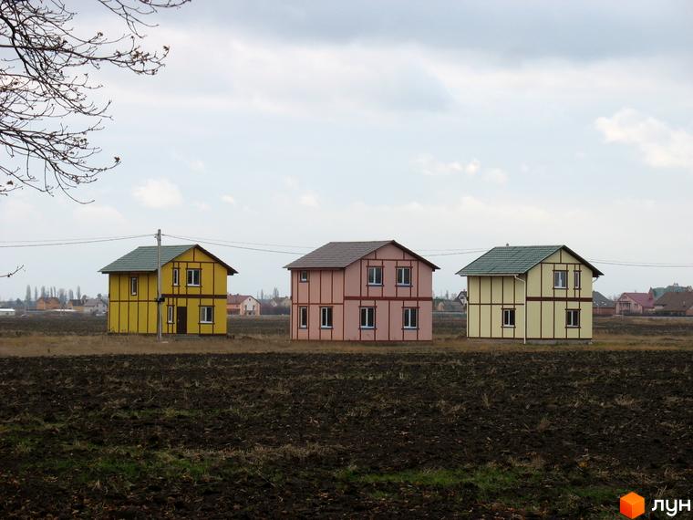 Три будинки з двома поверхами в Котеджному містечку Під Горою. Будинки пофарбовані в різні кольори, розташовані на тлі обробленого поля.