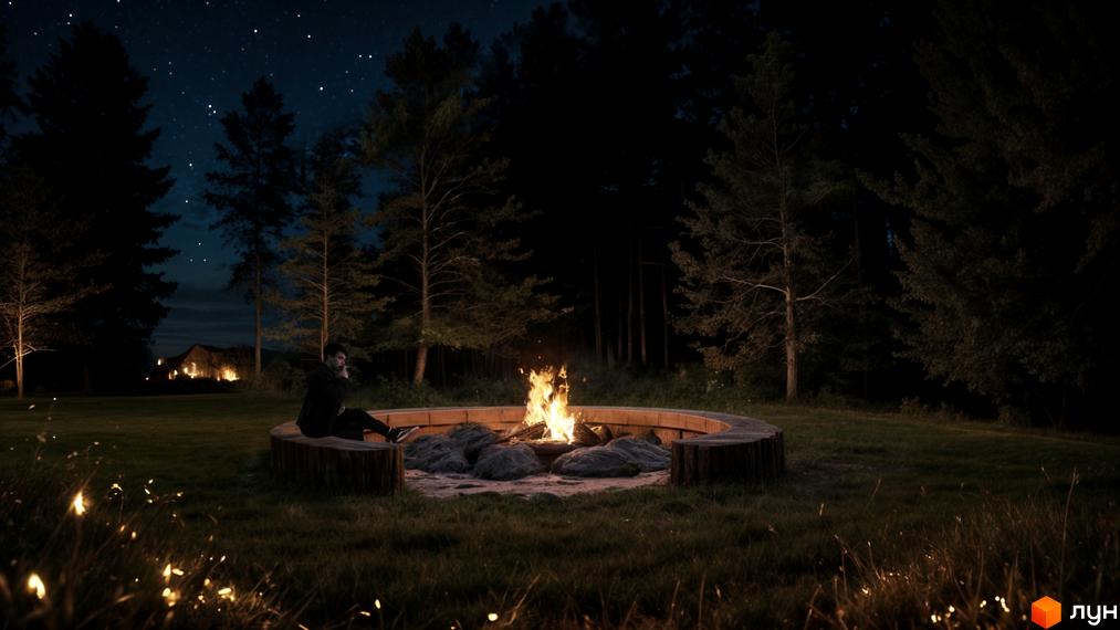 Людина сидить біля вогнища у Містечко котеджів. Навколо ліс, на небі видно зірки.