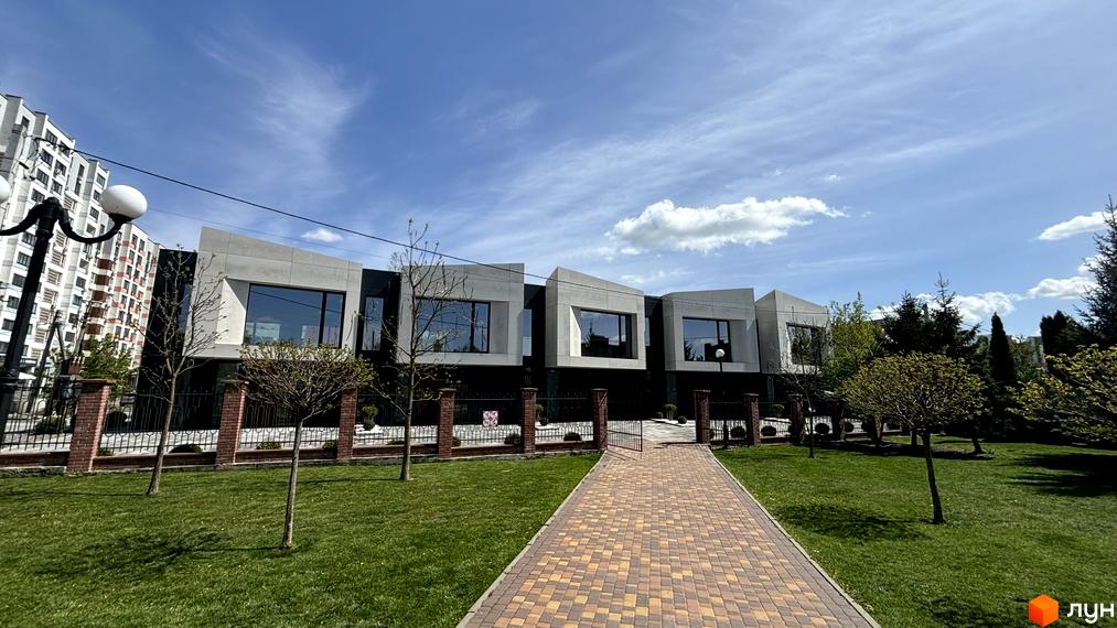 Житловий комплекс з незвичайним дизайном фасаду, розташований на вулиці Освіти. Зелена прибудинкова територія з доріжкою з бруківки.