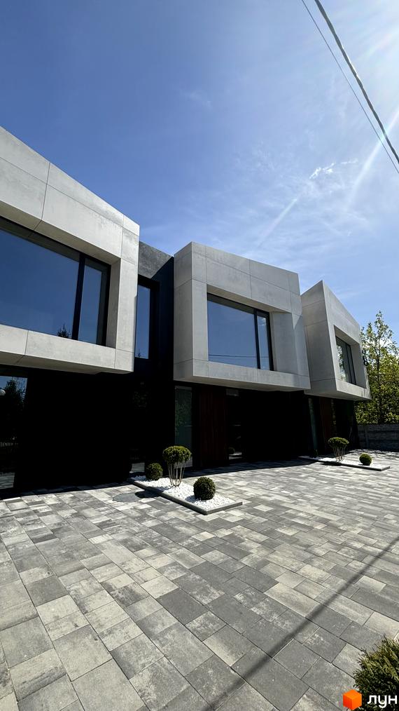 Фасад будинку з великими вікнами та бетонними блоками. На передньому плані бруківка та зелені насадження. ЖК вул. Освіти.