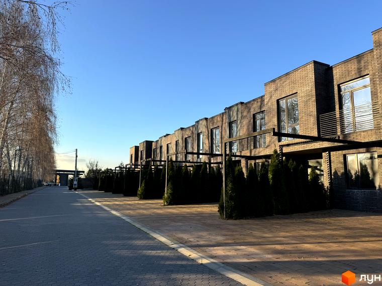 Цегляні будинки житлового комплексу Eastville з великими вікнами та терасами, перед будинками висаджені туї, поруч вимощена бруківкою доріжка.