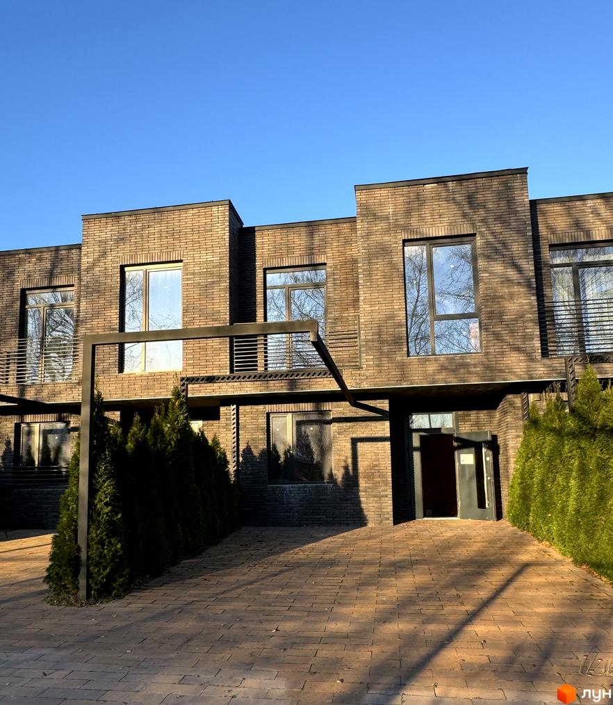 Цегляний будинок з великими вікнами та вхідними дверима. Перед будинком викладена бруківка, ростуть зелені кущі.