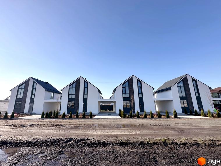 Білі будинки з темними вікнами та дахом в Котеджному містечку DESNA HOMES. Перед будинками розташована дорога та зелені насадження.