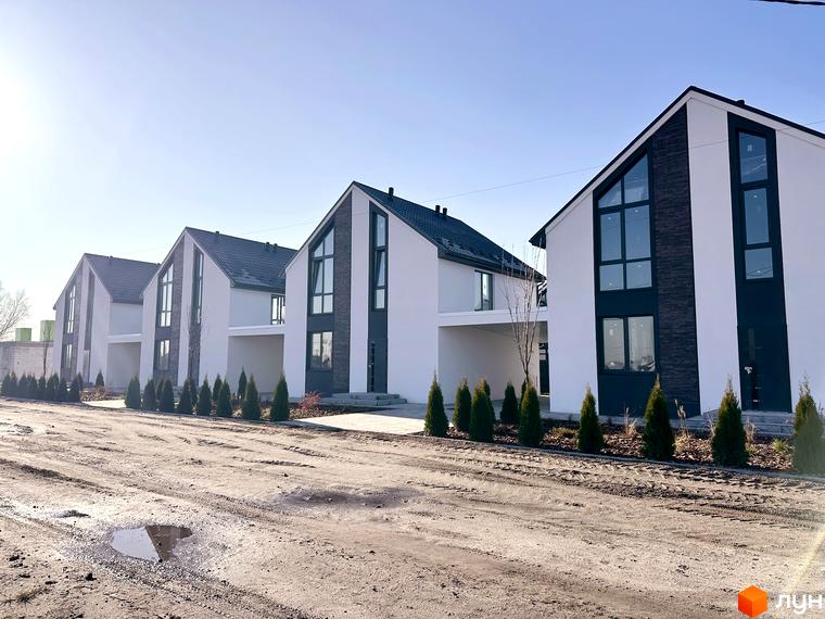 Білі будинки з темними дахами та великими вікнами у Котеджному містечку DESNA HOMES. На передньому плані — дорога з невеликими деревами.