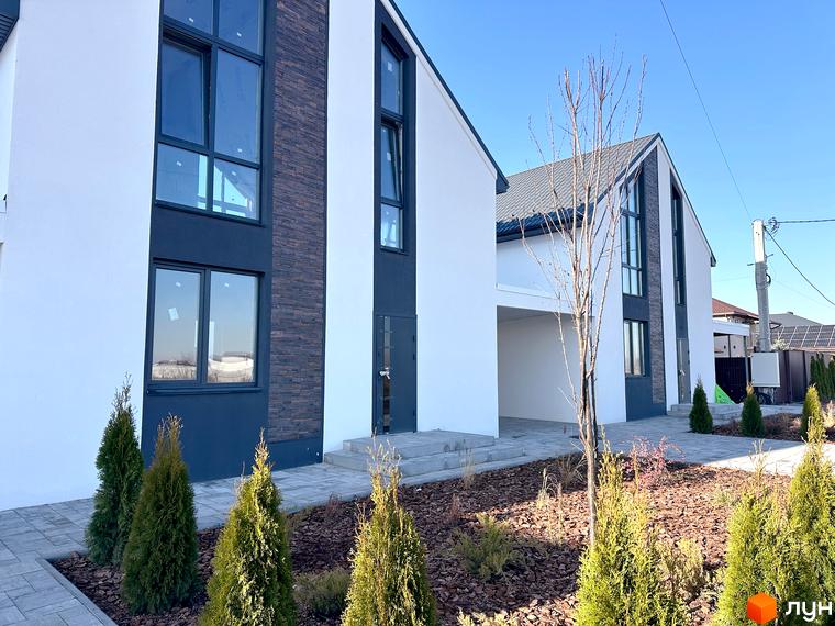 Фасад будинку в Котеджному містечку DESNA HOMES з великими вікнами та декоративною плиткою. На передньому плані зелені насадження та доглянута прибудинкова територія.