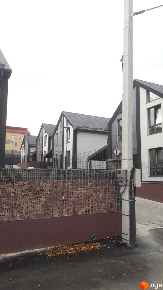 Ряд двоповерхових будинків з темними дахами та світло-темними фасадами на вул. Калинова. Перед ними габіонна огорожа та бруківка.