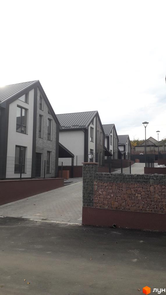 Ряд котеджів з темно-сірими дахами та світлими фасадами на вул. Калинова. Перед будинками бруковані доріжки та огорожі з габіонів.