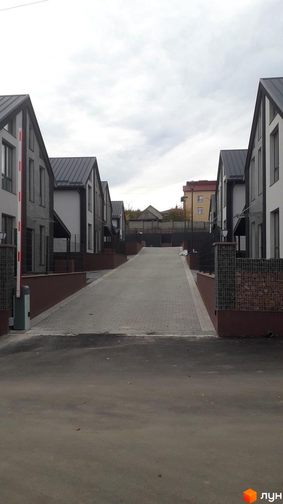 Ряд двоповерхових будинків з темними скатними дахами та світлими фасадами. Брукована дорога веде вгору, на в'їзді встановлено шлагбаум.