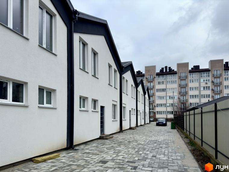 Ряд білих таунхаусів FreeSky з темними дахами та вікнами. Перед будинками викладена бруківкою доріжка.