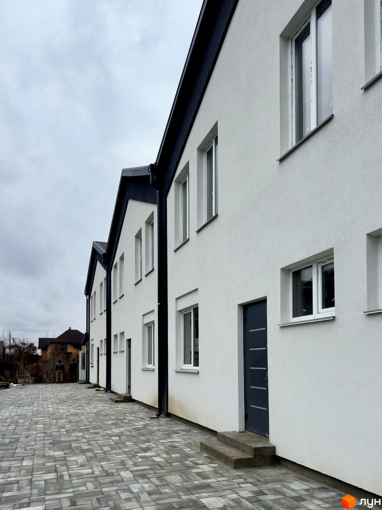 Ряд білих таунхаусів FreeSky з темними дахами та вікнами, перед якими викладена сіра бруківка.