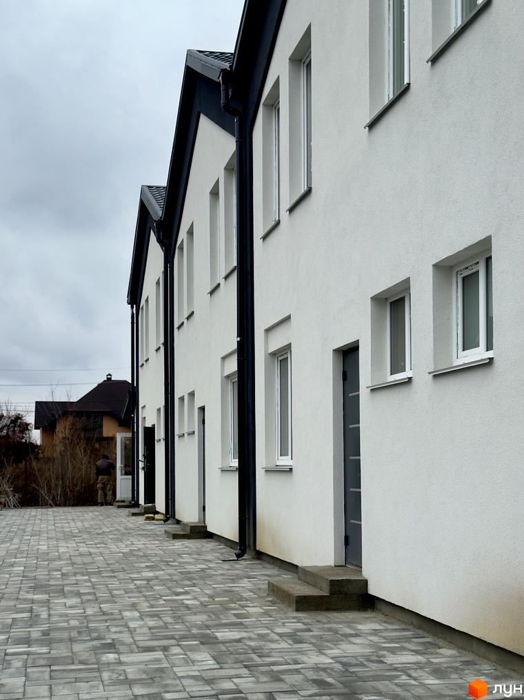 Ряд білих таунхаусів FreeSky з темними дахами та чорними водостічними трубами. Перед будинками вимощена сірою бруківкою доріжка.