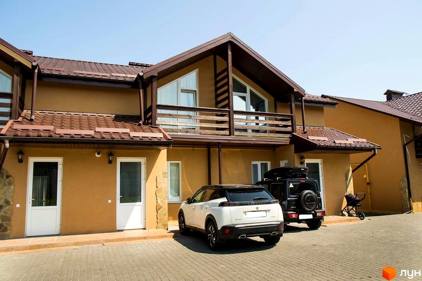 Таунхауси Андора: багатоквартирний будинок з коричневим дахом та балконами. На брукованій прибудинковій території припарковані два автомобілі.