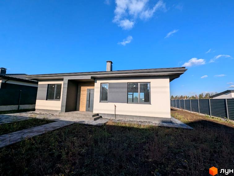 Одноповерховий будинок з бежевими стінами та темно-сірими акцентами, темний дах. Перед будинком вимощена доріжка, ділянка з ґрунтом та травою, видно огорожу.