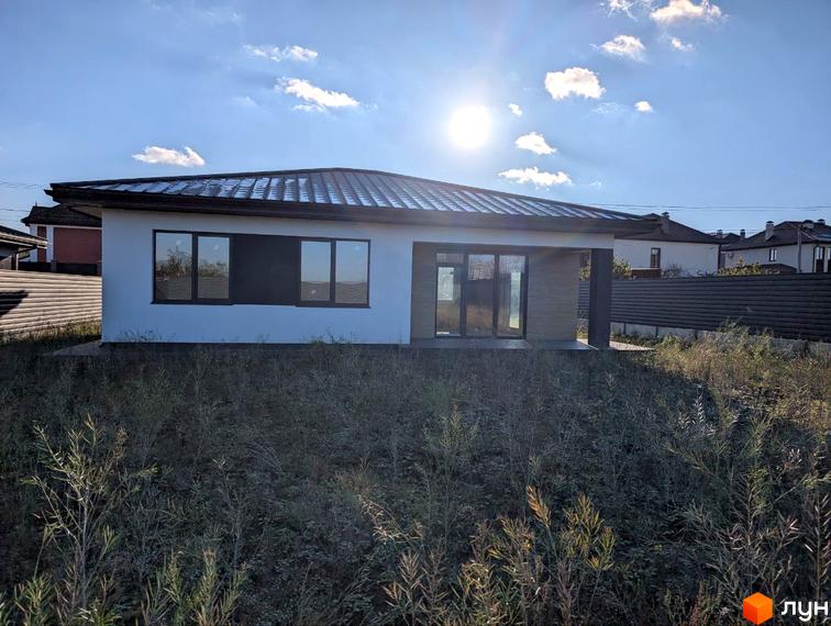 Одноповерховий будинок з темним дахом та білими стінами, великими вікнами, розташований на ділянці з високою травою на вул. Козацька.