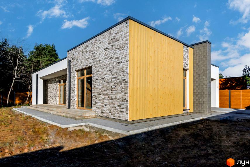 Фасад будинку Котеджного містечка LOTUS облицьований світлою цеглою та жовтими дерев'яними панелями, з великими вікнами та вимощеною доріжкою.