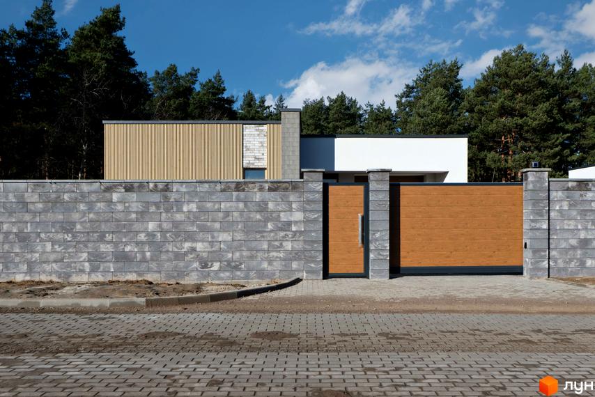 Котеджне містечко LOTUS: будинок з дерев'яним, білим та сірим фасадом, огороджений сірим блоковим парканом з дерев'яними воротами.