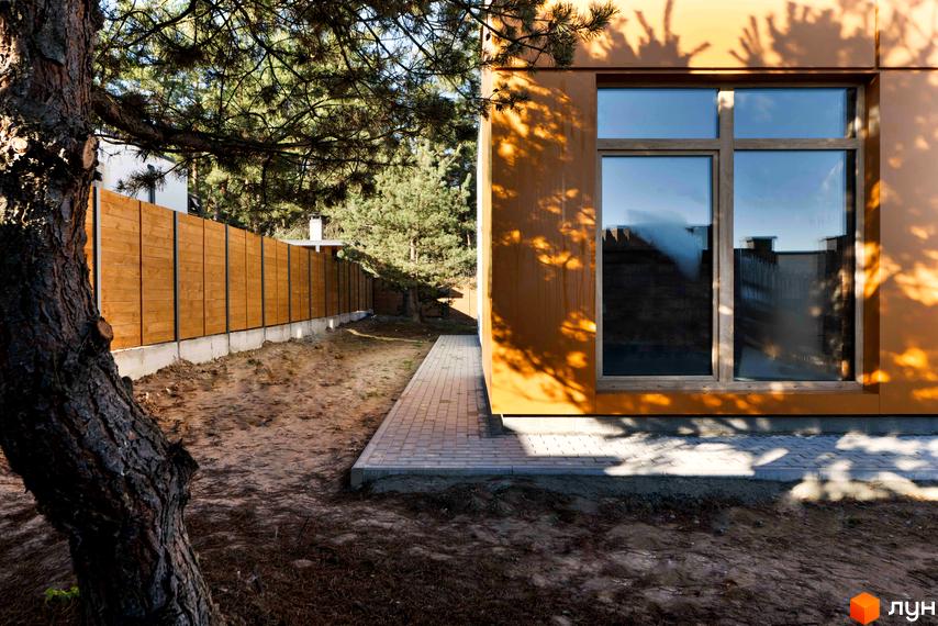 Будинок Котеджного містечка LOTUS з помаранчевим фасадом та великим вікном, поруч доріжка та дерев'яний паркан.