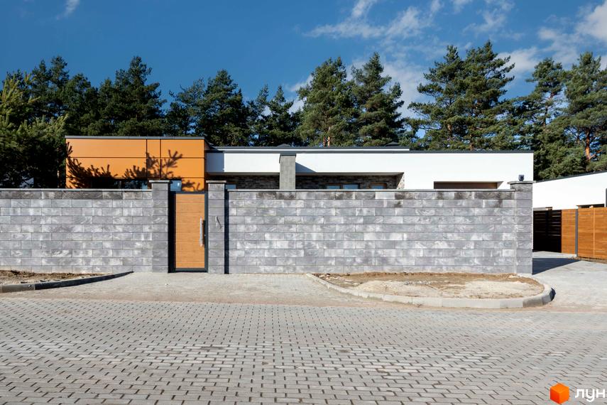 Фасад будинку Котеджного містечка LOTUS з помаранчевими та білими елементами. Перед будинком сірий цегляний паркан, дерев'яна брама та брукована дорога.