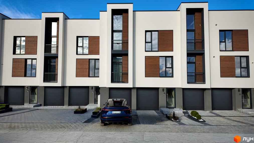 Таунхауси Motuz Hill з білими фасадами, дерев'яними вставками та великими вікнами. Перед будинками бруківка та доглянуті зелені насадження.