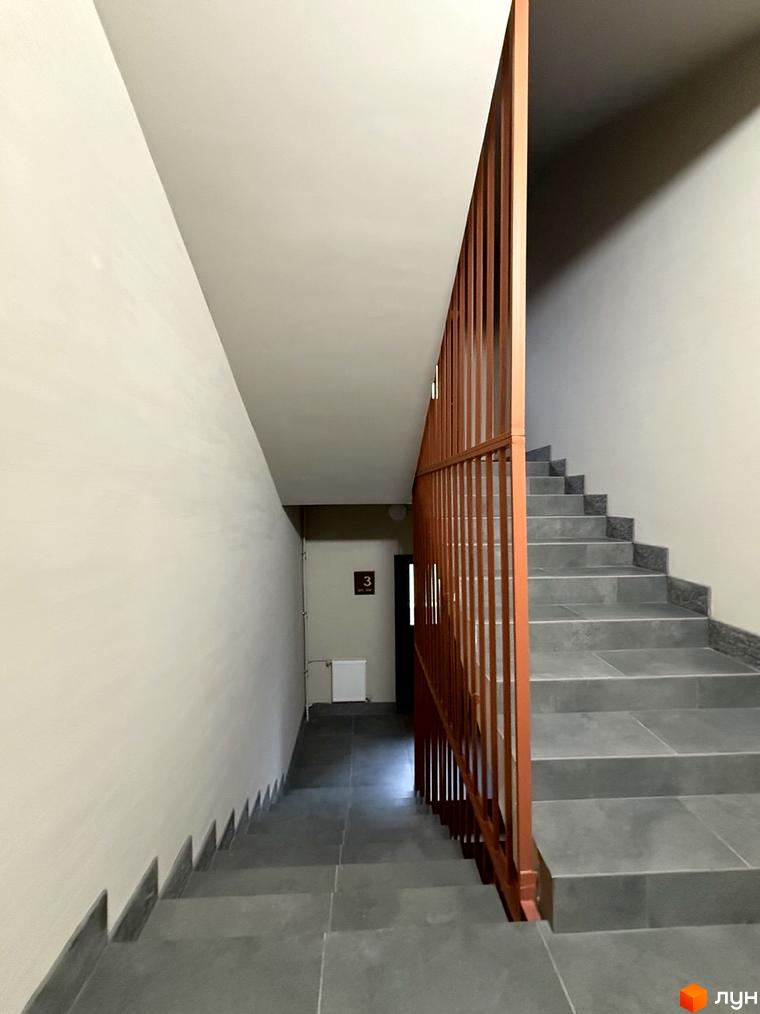 Сходи в під'їзді Житлового комплексу GRANIT: міцні сірі сходинки та вертикальні поручні, що забезпечують зручний доступ до поверхів.