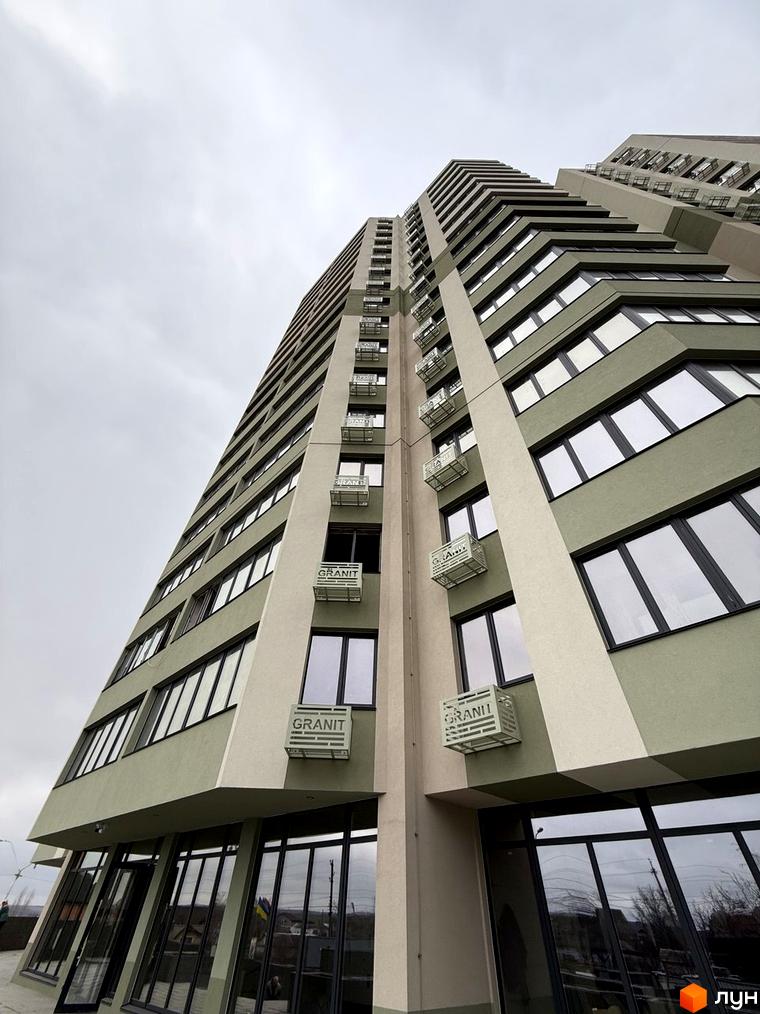 Багатоповерхова новобудова GRANIT з фасадами бежевого та оливкового кольорів, великими вікнами та зовнішніми блоками. На першому поверсі розташовані великі вітрини.
