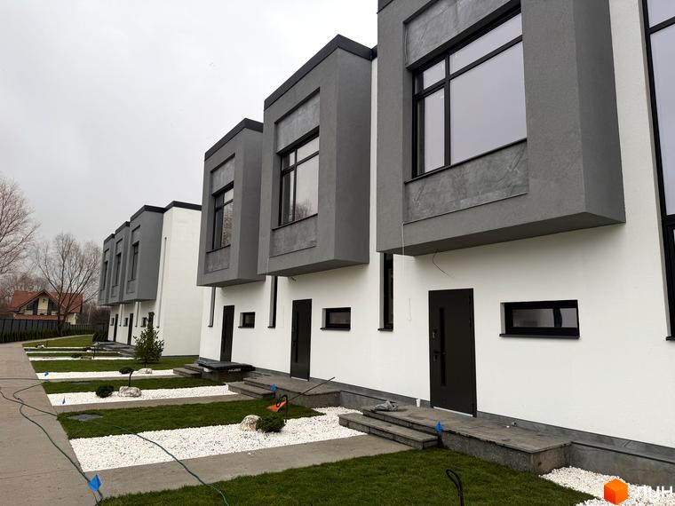 Ряд таунхаусів 11Dreams з білими фасадами та сірими верхніми блоками з великими вікнами. Прибудинкова територія має газони, білі камені та доріжки.