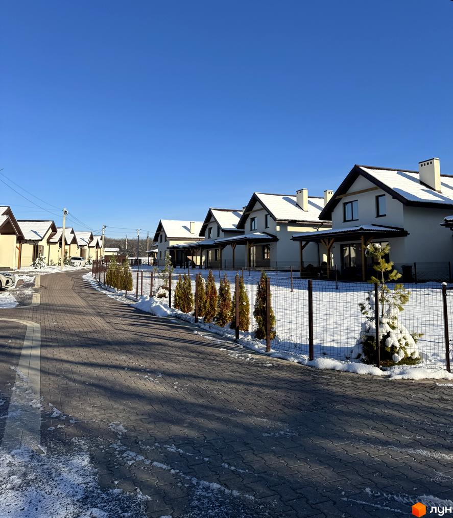 Котеджне містечко Буде Дім. Деревач: світлі будинки із засніженими дахами. Брукована доріжка, молоді дерева вздовж огорожі та сніг на прибудинковій території.