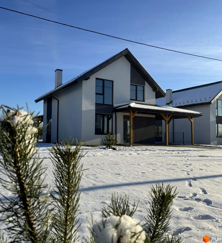 Двоповерховий будинок Котеджного містечка Буде Дім. Годовиця SPA з білим та темно-сірим фасадом і дерев'яним навісом. Прибудинкова територія вкрита снігом зі слідами.