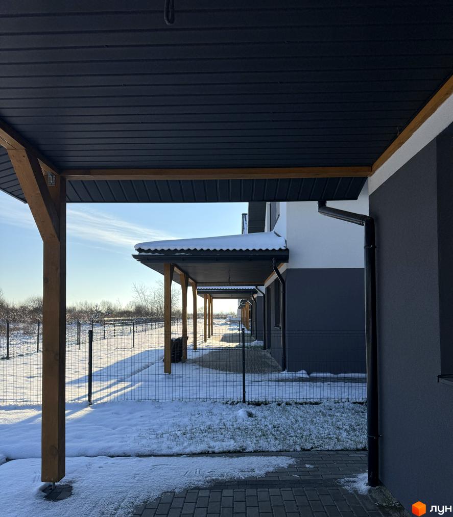 Фасади будинків Котеджного містечка Буде Дім. Годовиця SPA в темно-сірих та білих тонах з дерев'яними навісами. Прибудинкова територія засніжена, з огорожею та деревами.