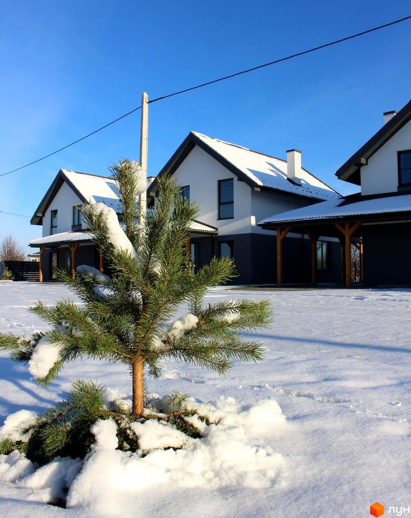 Котеджне містечко Буде Дім. Годовиця SPA: біло-сірі будинки з темними дахами, вкритими снігом. Засніжена територія з молодою ялинкою на передньому плані.