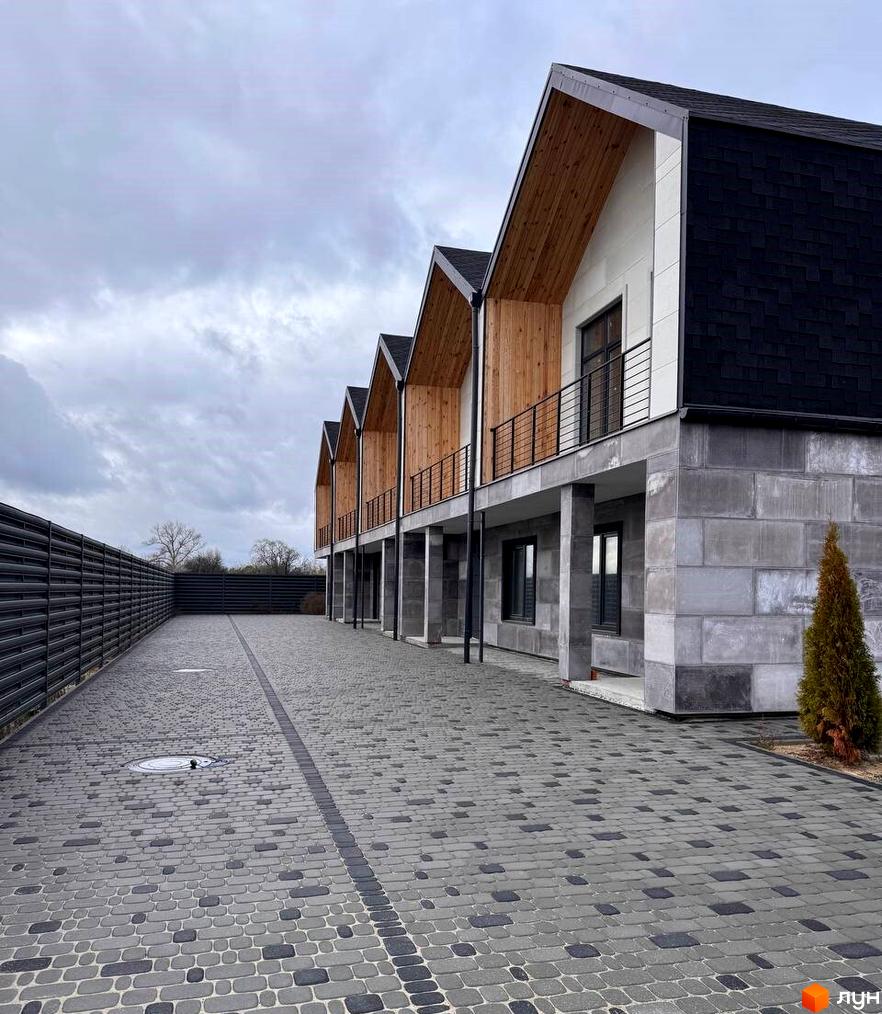 Таунхауси Riverium з темними дахами, дерев'яними елементами та балконами. Дорога викладена бруківкою, поруч темний паркан.