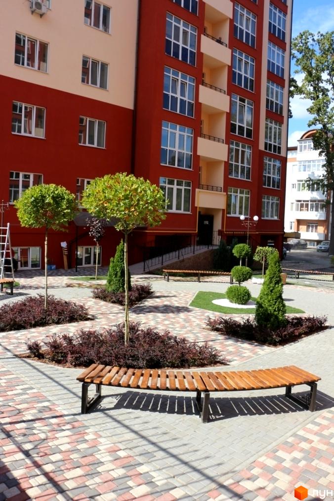 Житловий комплекс Green Life з фасадом червоного кольору. На прибудинковій території висаджені дерева та кущі, встановлені лавки.