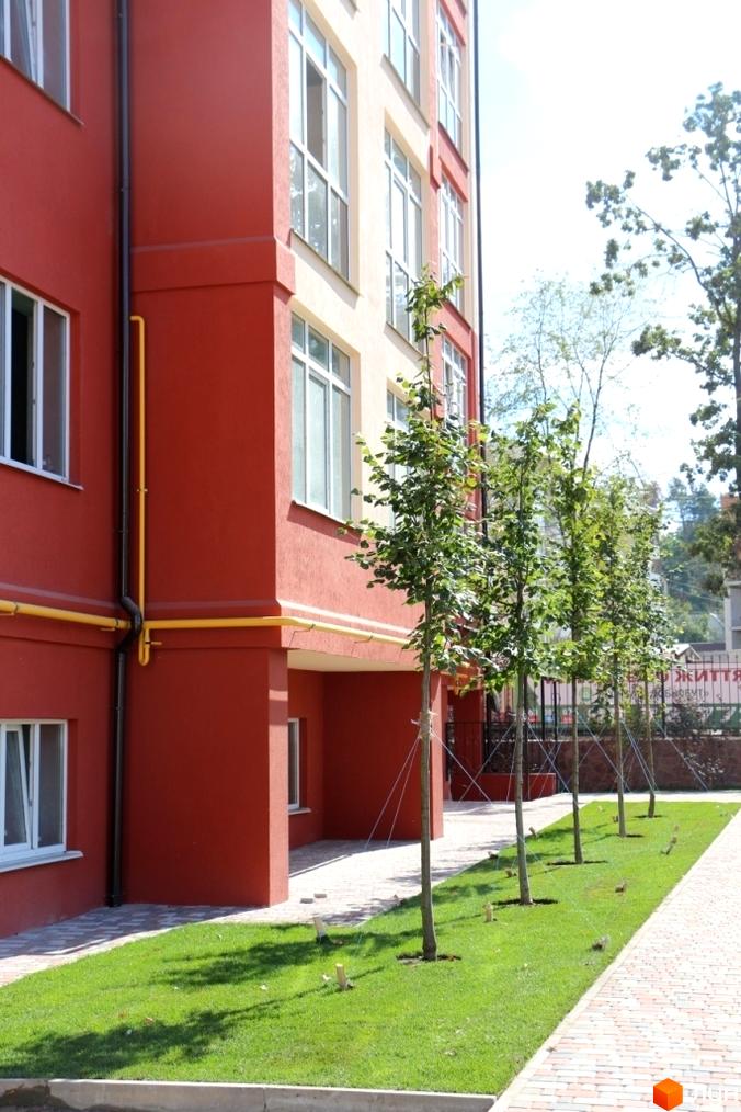 Житловий комплекс Green Life. Червоний фасад будівлі з великими вікнами. Біля будинку доглянута зелена зона з деревами та тротуар.