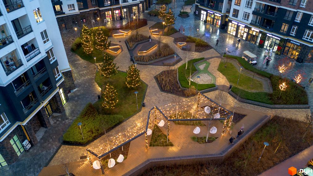 Житловий комплекс Синергія Сіті з житловими будинками, комерційними приміщеннями на першому поверсі та святково освітленим двором з алеями, лавками та ялинками.