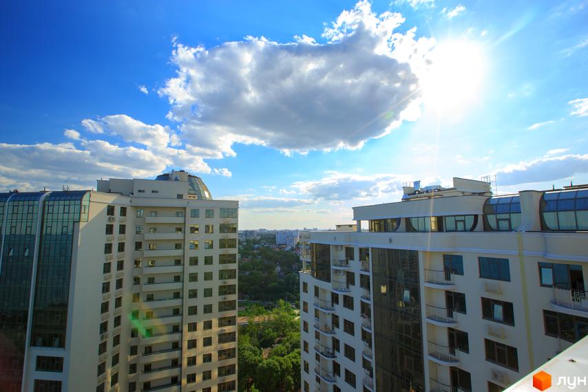 Високі будинки ЖК Друга Перлина на тлі блакитного неба з хмарами. Видно панорамні вікна та балкони, а також зелені насадження навколо.