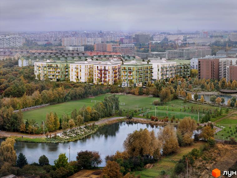 Багатоповерхові будинки Житлового комплексу VERO з білими, світло-зеленими та цегляними фасадами. Поруч зелені футбольні поля, озеро та осінні дерева.