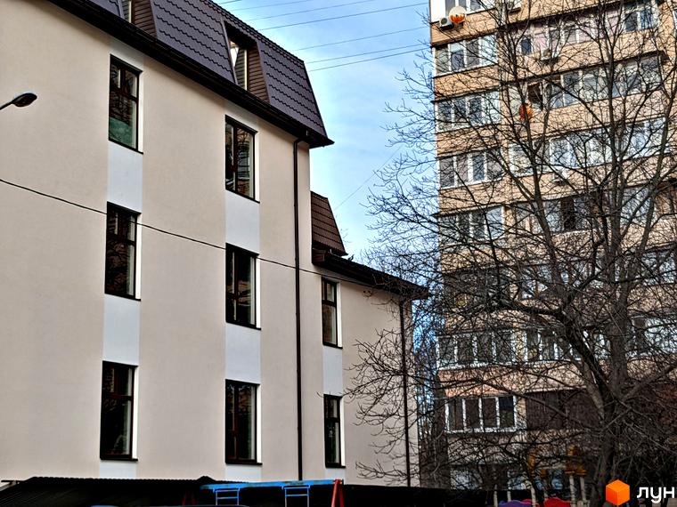 Зображення житлового комплексу на вул. Яслинській, 3: світлий будинок з мансардним дахом, поруч дерево та інша будівля.