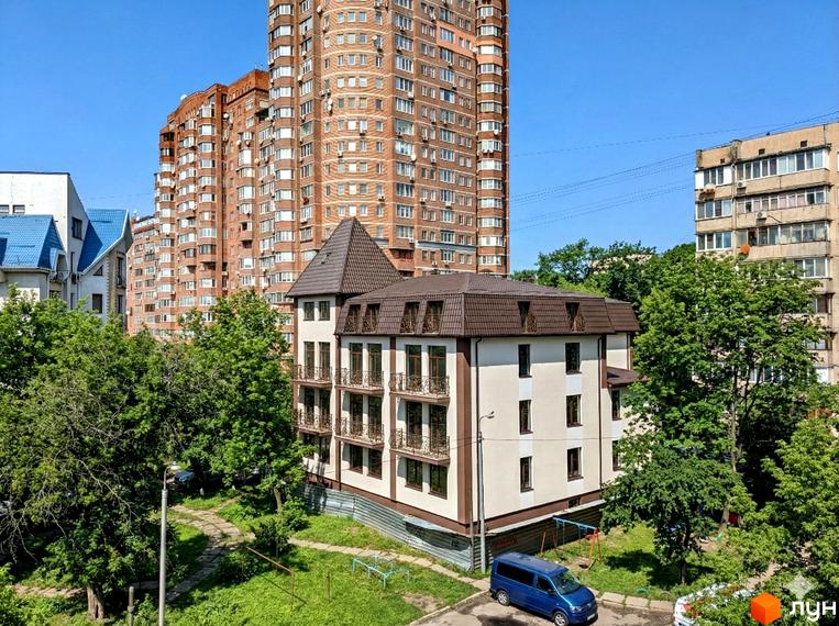 Житловий комплекс на вул. Яслинська, 3 має світлі фасади, коричневий дах та балкони з кованими перилами. Навколо будинку зелені дерева, доріжки та дитячий майданчик.