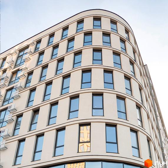 Фасад житлового комплексу Kniahynyn-Center з вигнутими лініями, світлими стінами та численними вікнами. На стінах видно зовнішні блоки кондиціонерів.