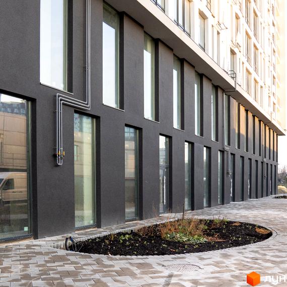 Фасад Житлового комплексу Kniahynyn-Center виконаний у темних тонах з великими вікнами. Прибудинкова територія має мощену доріжку та круглу клумбу.