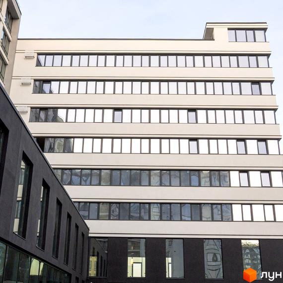 Житловий комплекс Kniahynyn-Center: світлий багатоповерховий будинок з рівними рядами вікон та темною прибудовою на передньому плані.