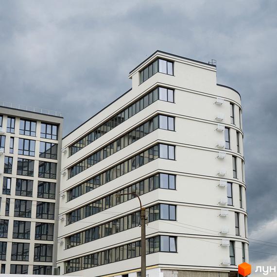 Житловий комплекс Kniahynyn-Center: багатоповерхові будинки зі світлим та сірим фасадами, великими вікнами на тлі хмарного неба.