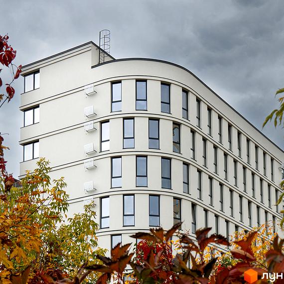 Житловий комплекс Kniahynyn-Center з білим вигнутим фасадом та прямокутними вікнами. На передньому плані осінні дерева.