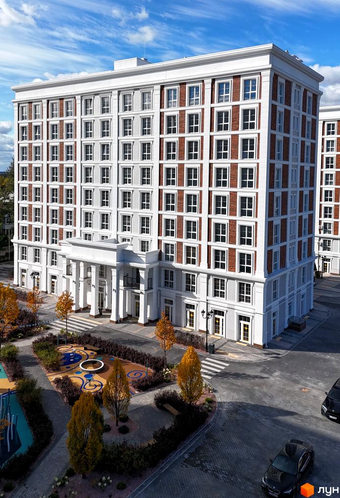 Житловий комплекс OXFORD: багатоповерховий будинок з білим фасадом та цегляними вставками, великими вікнами та колонним входом. Прибудинкова територія з дитячим майданчиком та деревами.