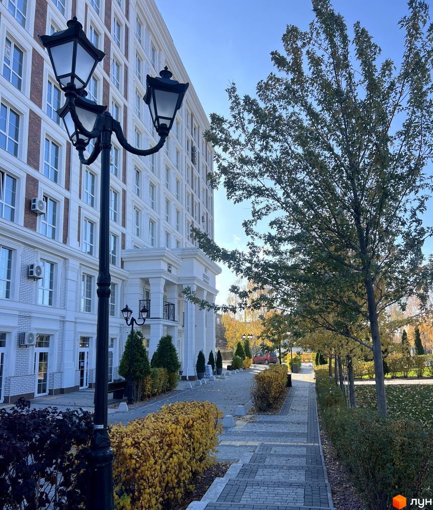 Житловий комплекс OXFORD з білими фасадами та цегляними вставками. Прибудинкова територія з деревами, кущами та бруківкою.