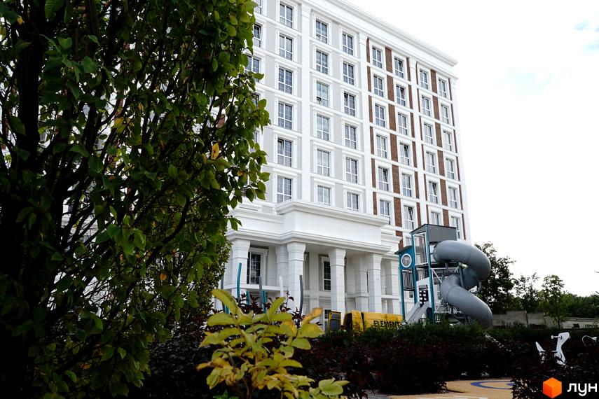 Багатоповерховий будинок Житлового комплексу OXFORD з білими фасадами та коричневими вставками. Поруч дитячий майданчик з гірками та зелені насадження.