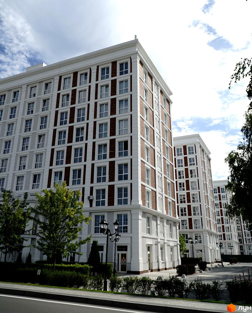 Житловий комплекс OXFORD: багатоповерхові будинки з білими фасадами, цегляними вставками та великими вікнами. Перед ними зелена зона з деревами.